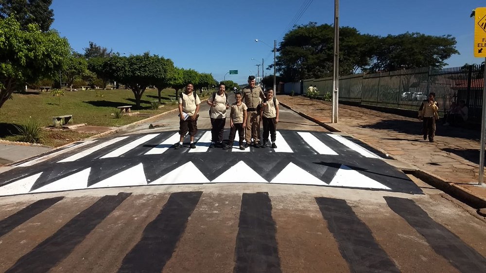 Policial militar com alunos sobre uma faixa de pedestre elevada: mais segurança próximo das escolas